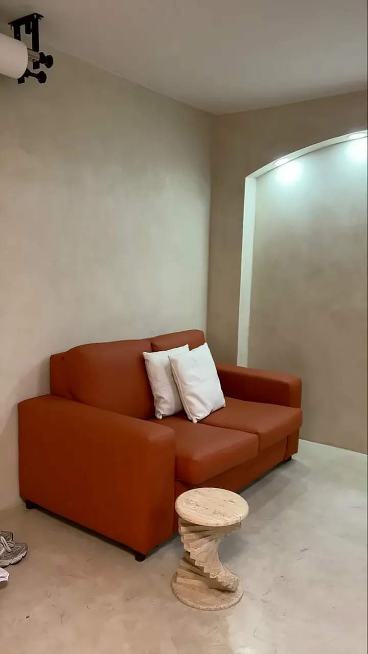 Sofá terracota con cojines blancos contra la pared greige, junto a un arco redondo.
